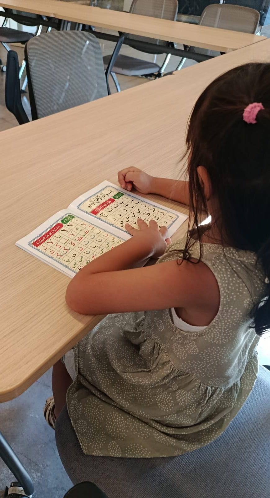 A girl sounding out letters from her workbook