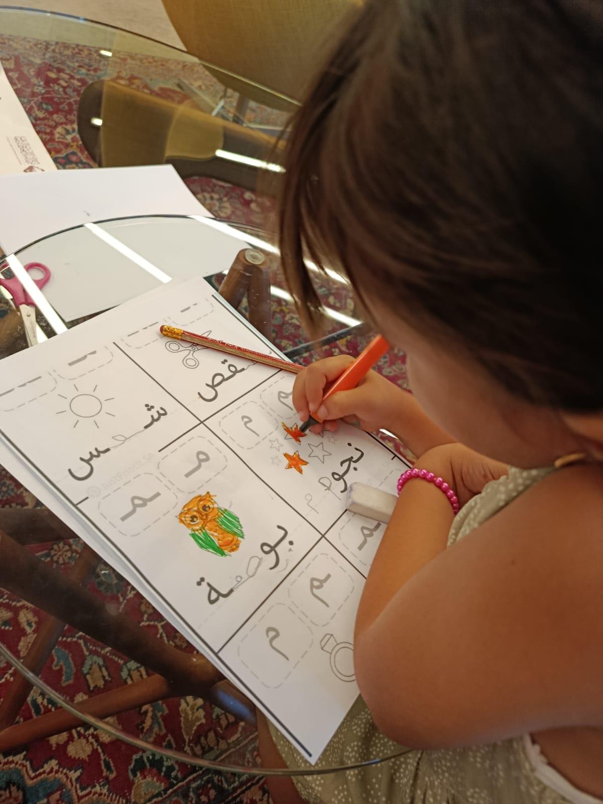 A young student colouring and tracing Arabic letters