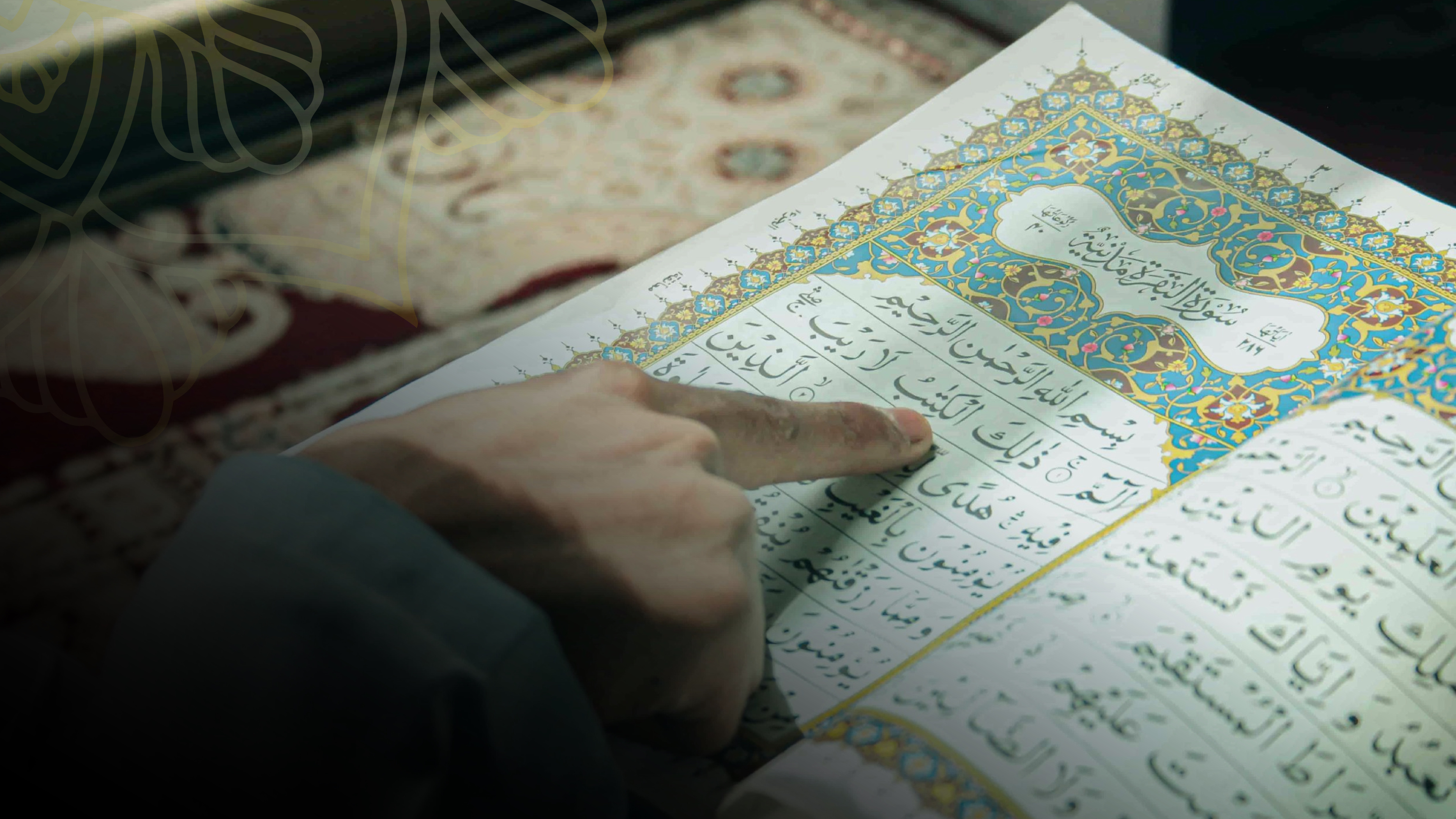 A finger following a line of an illuminated muṣḥaf open at Sūrat al-Baqarah